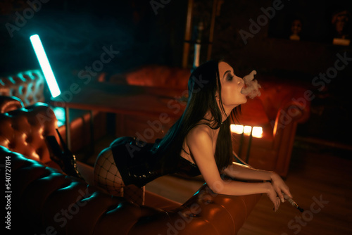 A sexy and beautiful woman enjoys a hookah in a nightclub. Glamorous clothes and neon lights.