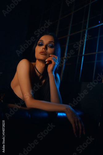 A sexy and beautiful woman enjoys a hookah in a nightclub. Glamorous clothes and neon lights.