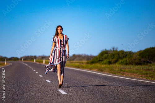 a beautiful long-haired girl in a long dress walks along a road in the desert in western australia  a beautiful girl lost in the middle of nowhere