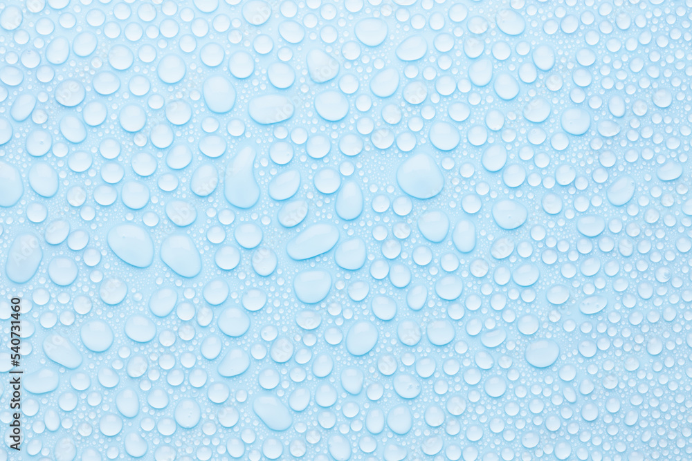 Water drops on cold soft light blue background as pattern of different round glossy shine drops as dew, texture, top view.