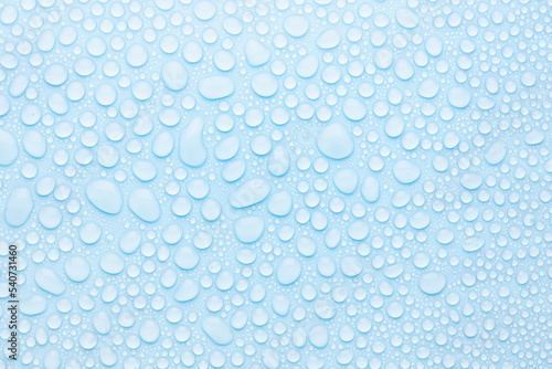 Water drops on cold soft light blue background as pattern of different round glossy shine drops as dew, texture, top view.