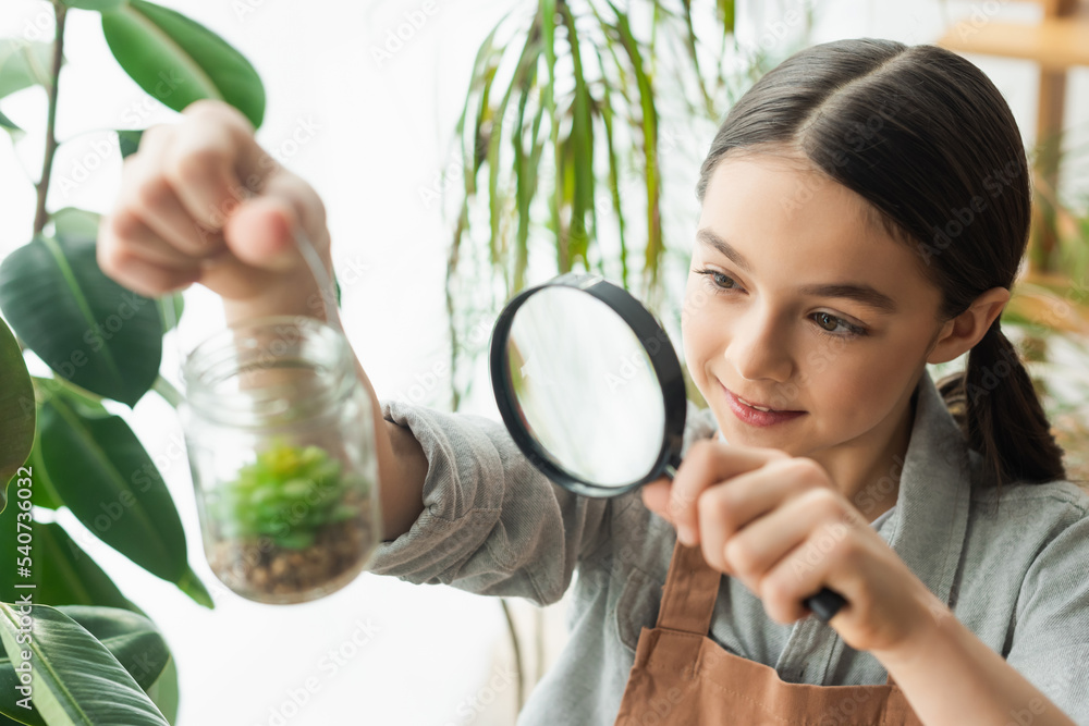 Smiling girl holding magnifying glass and blurred jar with succulent at home. Smiling girl holding magnifying glass and blurred jar with succulent at home.