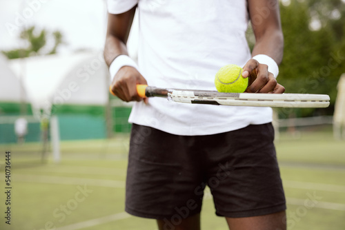 Close-up of the of African-looking man holding tennis racket and ball. Tennis player is wearing white T-shirt and black shorts and has wristbands on hands. He is playing tennis and is ready to serve.