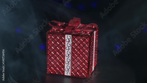Gift red box slowly rotates on a black background in a haze and with festive lights
