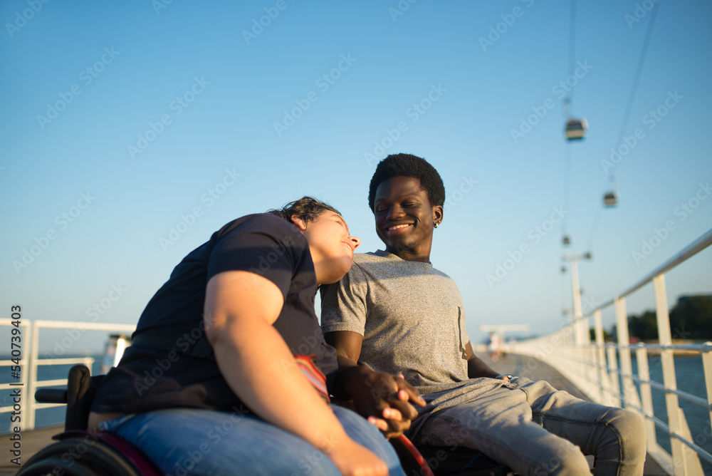 Warm multicultural couple spending day together. African American man and Caucasian woman in wheelchairs, looking each other, holding hands. Love, affection, happiness concept Warm multicultural couple spending day together. African American man and Caucasian woman in wheelchairs, looking each other, holding hands. Love, affection, happiness concept
