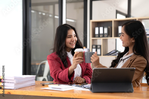 Two young Asian businesswomen show joyful expression of success at work smiling happily with a laptop computer in a modern office.