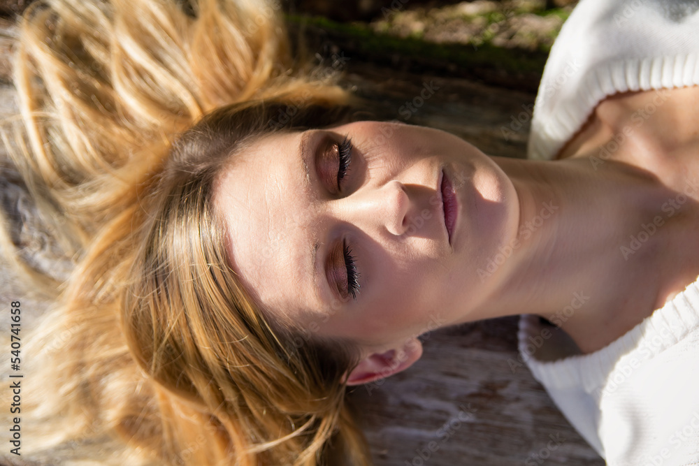 Portrait of young blonde caucasian woman laying on tree with closed eyes Portrait of young blonde caucasian woman laying on tree with closed eyes