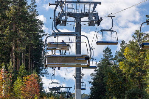 Ski lift in mountain autumn forest. Climbing uphill on a cable car. Open cable car line. Chairlift against autumn forest. Ski chair lift at off season in Bobrovy log, Krasnoyarsk, Russia photo