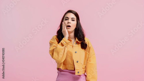 exhausted young woman in orange denim jacket looking at camera isolated on pink