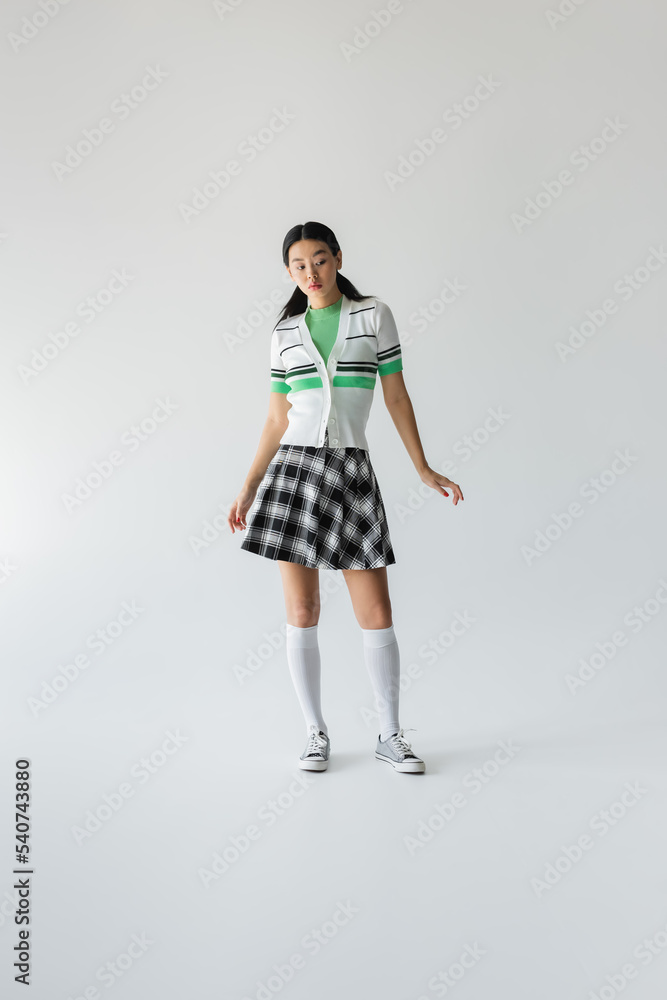 Full length of young asian woman in skirt and knee socks standing on grey background Full length of young asian woman in skirt and knee socks standing on grey background