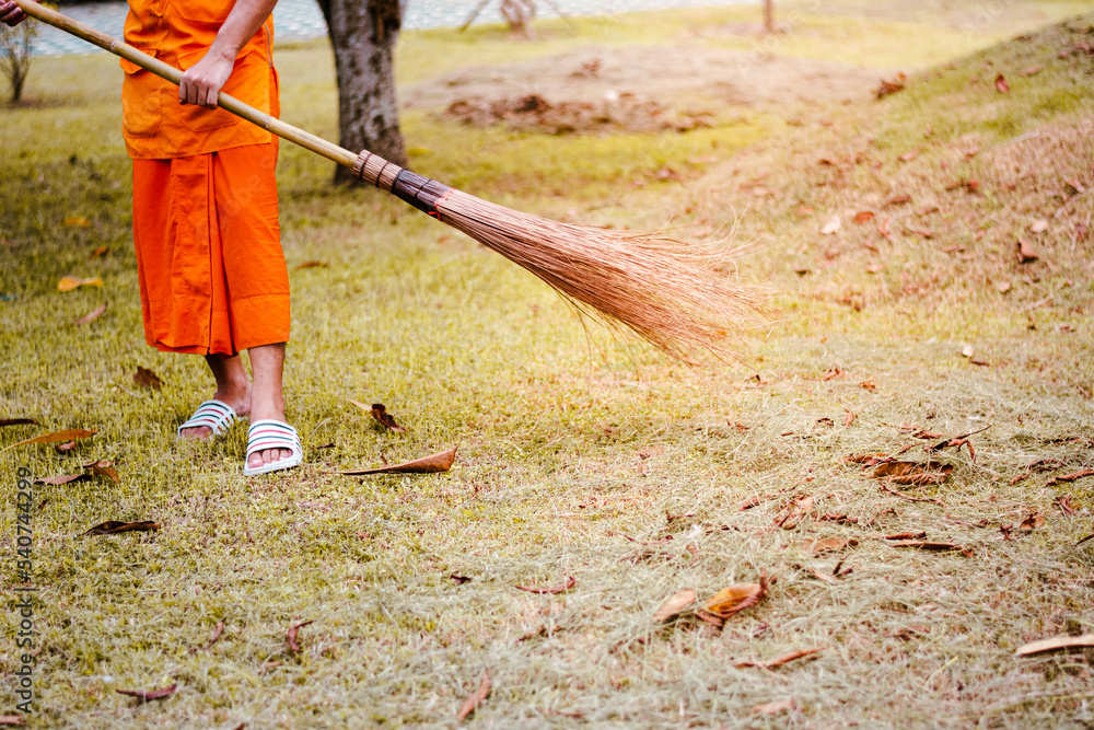 Naklejka premium The monk sweeps leaves to collect trash in the temple courtyard.