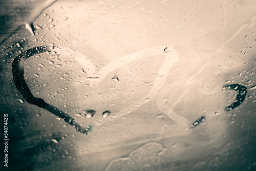 Two heart drawings by finger on steamy car windshield glass with raindrops