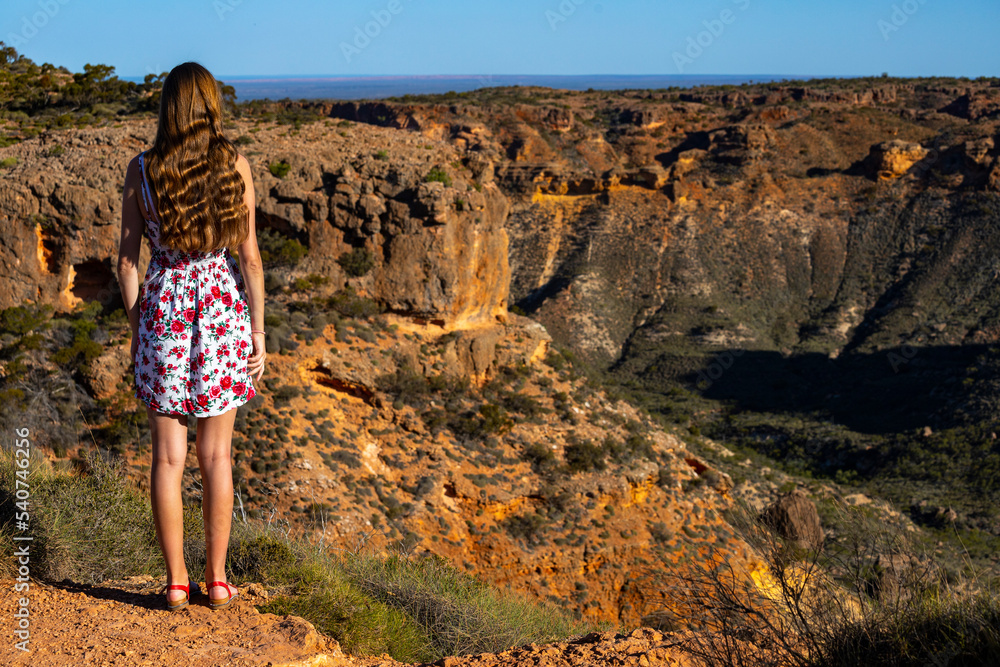 a beautiful girl in a short white dress stands on top of a mountain above a massive gorge in western australia at sunset, hiking in cape range national park near exmouth