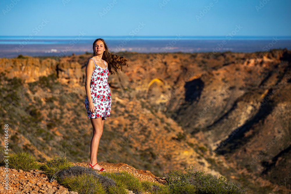 a beautiful girl in a short white dress stands on top of a mountain above a massive gorge in western australia at sunset, hiking in cape range national park near exmouth