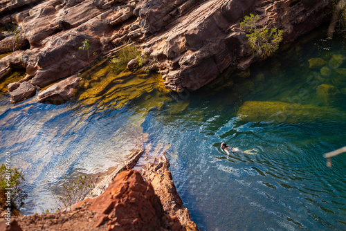 a long-haired girl in a white bikini takes a refreshing dip in a rock pool in karijini national park in western australia, an oasis in the middle of the desert in the australian outback