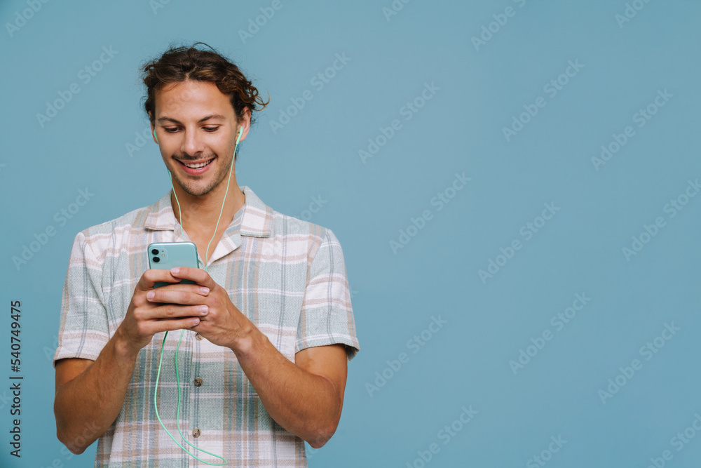 Ginger european man in earphones smiling and using cellphone