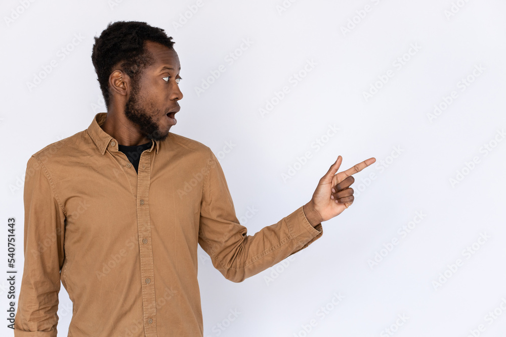 Astonished man pointing aside. Male African American model in black T-shirt and brown shirt pointing and looking at something with surprise. Portrait, studio shot, advertising concept Astonished man pointing aside. Male African American model in black T-shirt and brown shirt pointing and looking at something with surprise. Portrait, studio shot, advertising concept
