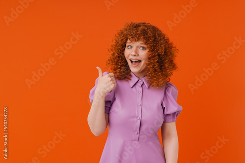 White excited woman with ginger hair showing thumb up at camera