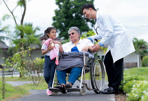A young asian doctor and a young girl take care of an elderly middle eastern woman in a wheelchair.