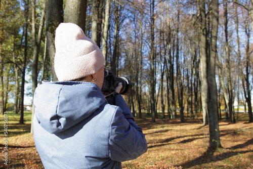 Photographer woman with DSLR camera and zoom lens take photos in autumn Park on yellow fall leaves