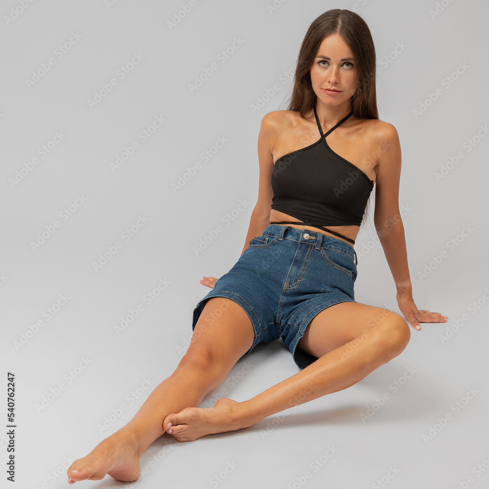 A beautiful girl, in a black top, sits on a gray background.