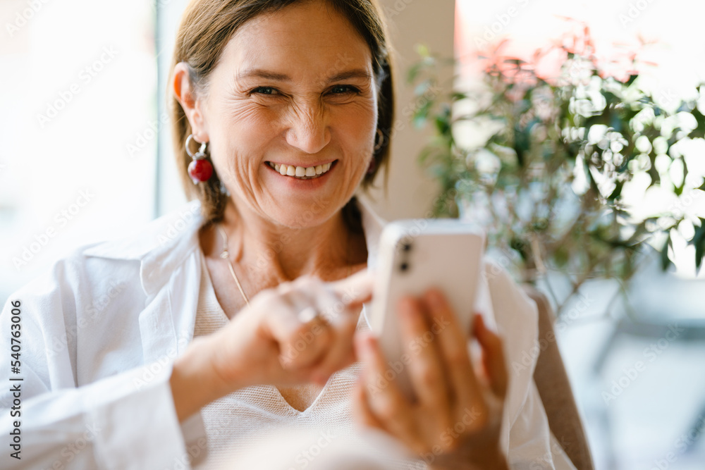White mature woman using cellphone while sitting in cafe indoors White mature woman using cellphone while sitting in cafe indoors