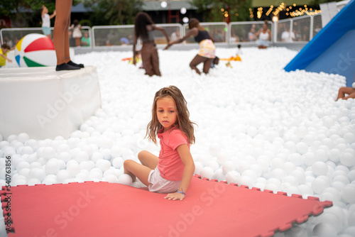 Happy little girl playing white plastic balls pool in amusement park. photo