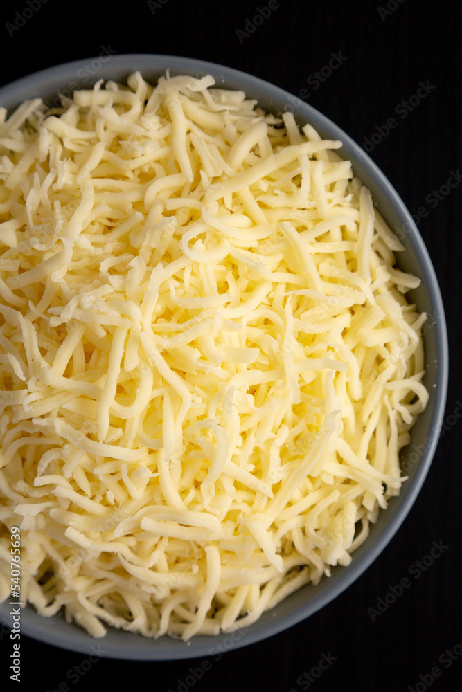 Shredded Mozzarella Cheese in a Bowl on a black surface, top view. Flat lay, overhead, from above. Shredded Mozzarella Cheese in a Bowl on a black surface, top view. Flat lay, overhead, from above.