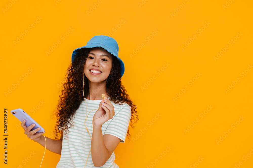 Curly brunette woman in earphones smiling and using cellphone Curly brunette woman in earphones smiling and using cellphone