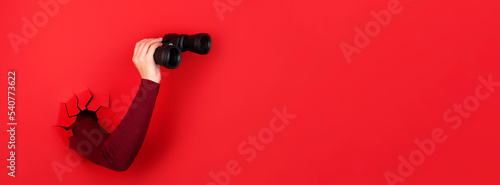 Fotografia binoculars in hand over red background, panoramic layout