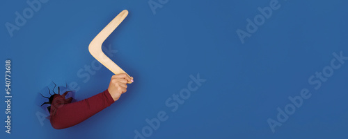 hand holding boomerang  over blue background, panoramic layout photo