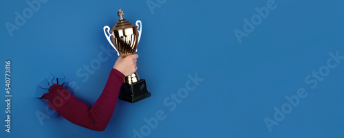 golden sports cup in hand over blue background, panoramic layout photo