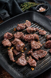Diced beef cubes roasting in a grill pan for stew or goulash. Dark background. Top view