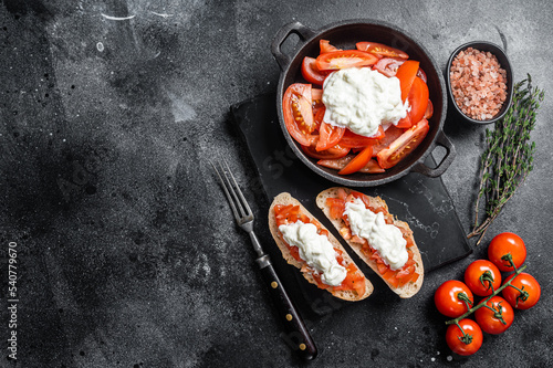 Crusty Bruschettas toasts with stracciatella cheese, chopped tomatoes and thyme. Black background. Top view. Copy space