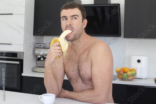Fotografia Shirtless man eating a banana in the kitchen