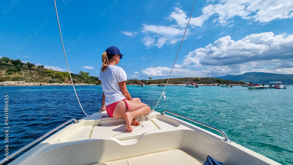 Woman sitting on bow of luxury boat in the blue lagoon of Vourvourou on peninsula Sithonia, Chalkidiki (Halkidiki), Greece, Europe. Tropical crystals clear turquoise water. Summer vacation atmosphere