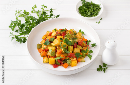 Vegetable stew with zucchini, carrots, potatoes and parsley on a white plate on a light gray background