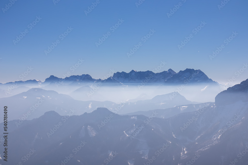 Fototapeta premium Scenic view from summit of Freiberg on misty snow capped mountain peaks in Karawanks mountains, Carinthia, Austria. Winter wonderland on sunny day in Austrian Alps, Europe. Ski tour, snow shoe hiking