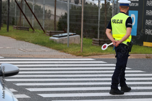 Policjant ruchu drogowego na przejściu dla pieszych kontroluje ruch pieszych. Przy radiowozie. 