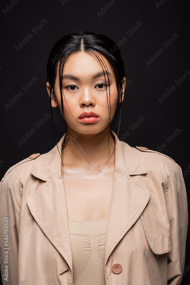 Portrait of asian woman in trench coat looking at camera isolated on black Portrait of asian woman in trench coat looking at camera isolated on black