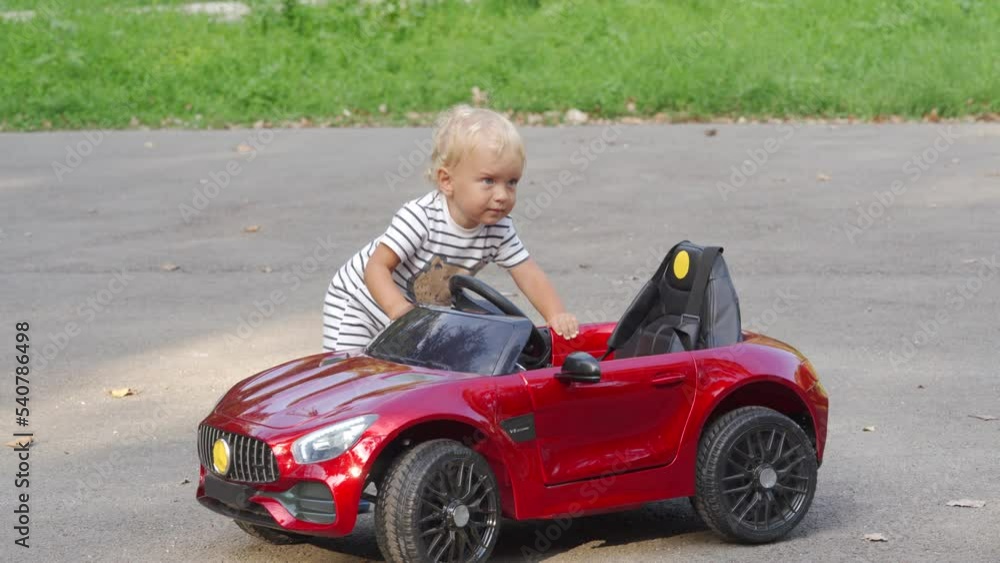 Little child boy playing with electric car toy for kids. 1.5 year old toddler pushing small electric car outdoors. Battery powered car with parent control. Little child boy playing with electric car toy for kids. 1.5 year old toddler pushing small electric car outdoors. Battery powered car with parent control.