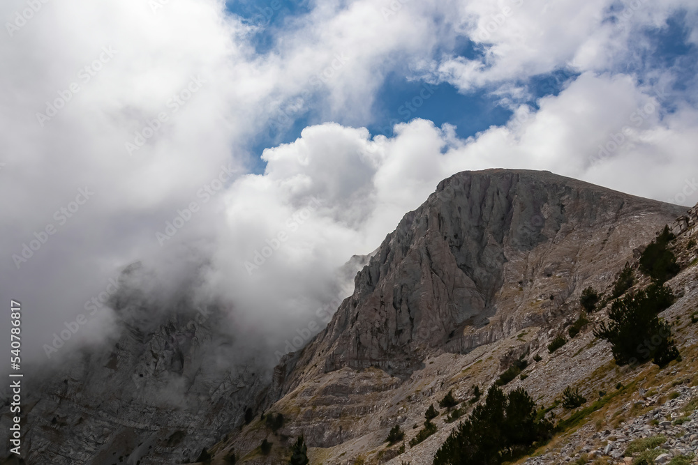 Panoramic view of the cloud covered slopes and rocky ridges of Pieria Mountains near Mount Olympus in Mt Olympus National Park, Thessaly, Greece, Europe. Trekking on hiking trail through mystical fog