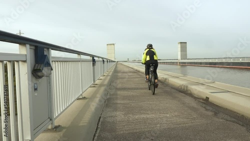 a couple of cyclists rides over a trough bridge where a water-filled canal crosses a natural river