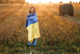 Ukrainian girl with a blue-yellow flag against the sky. War in Ukraine. Ukrainian Independence Day. Ukrainian girl stands with a flag of Ukraine in the middle of field against a sunset sky