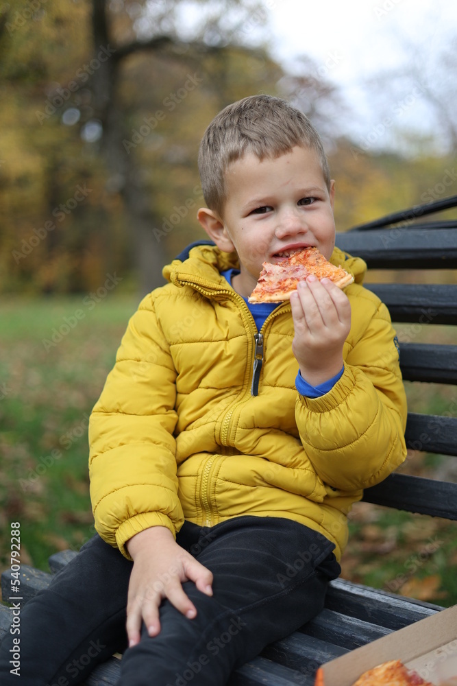 little child sitting on a bench and eating pizza little child sitting on a bench and eating pizza