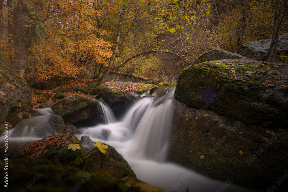 Long exposure of a waterfall of a river surrounded by autumn foliage. Scenic and relaxing image. River Po, Italy.