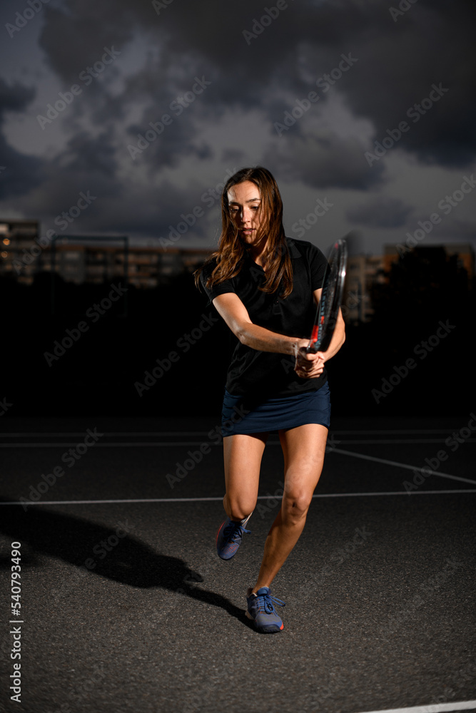 Woman with racket playing tennis on outdoor court at evening.