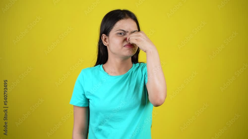 Portrait of young woman pinching nose with disgust on his face due to bad smell isolated over yellow background Portrait of young woman pinching nose with disgust on his face due to bad smell isolated over yellow background