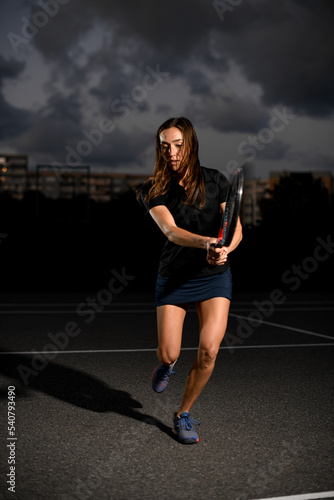 Fototapeta Naklejka Na Ścianę i Meble -  Woman with racket playing tennis on outdoor court at evening.
