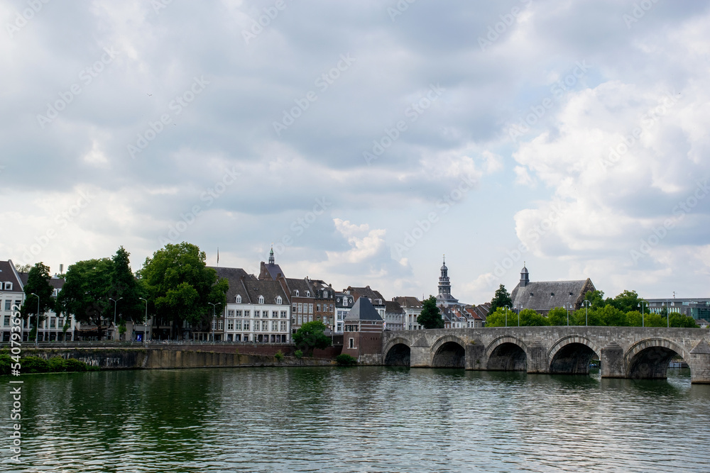urban cityscape off the city Maastricht in the netherlands, clouded sky. Skyline with river in the front and stone bridge on the right. Travel destination european culture historic architecture. 
